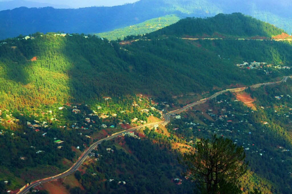 Lush green trees with a mountain backdrop under a cloudy sky, as gentle sun rays break through the clouds and illuminate the landscape.